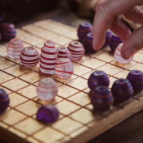 The image shows a replica Hnefatafl set, with the pieces made from glass. The player is moving a piece. Based ona  find from Birka, Sweden.