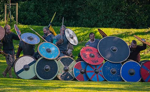 The image shows warriors defending against arrows by forming a shiled wall.