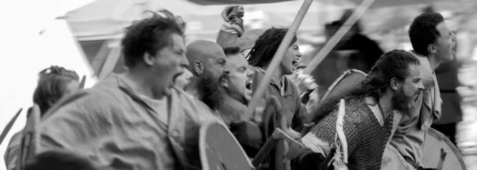 This black and white image shows a group of fierce warriors charging their enemy with their weapons held high and screaming a warcry.