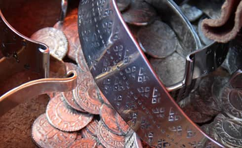 The image shows an assortment of silver coins and arm rings used by the Vikings to trade and buy goods.