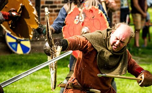 This image shows a sword impacting against a shield, sending splinters flying while the warrior holding the shield looks very worried.